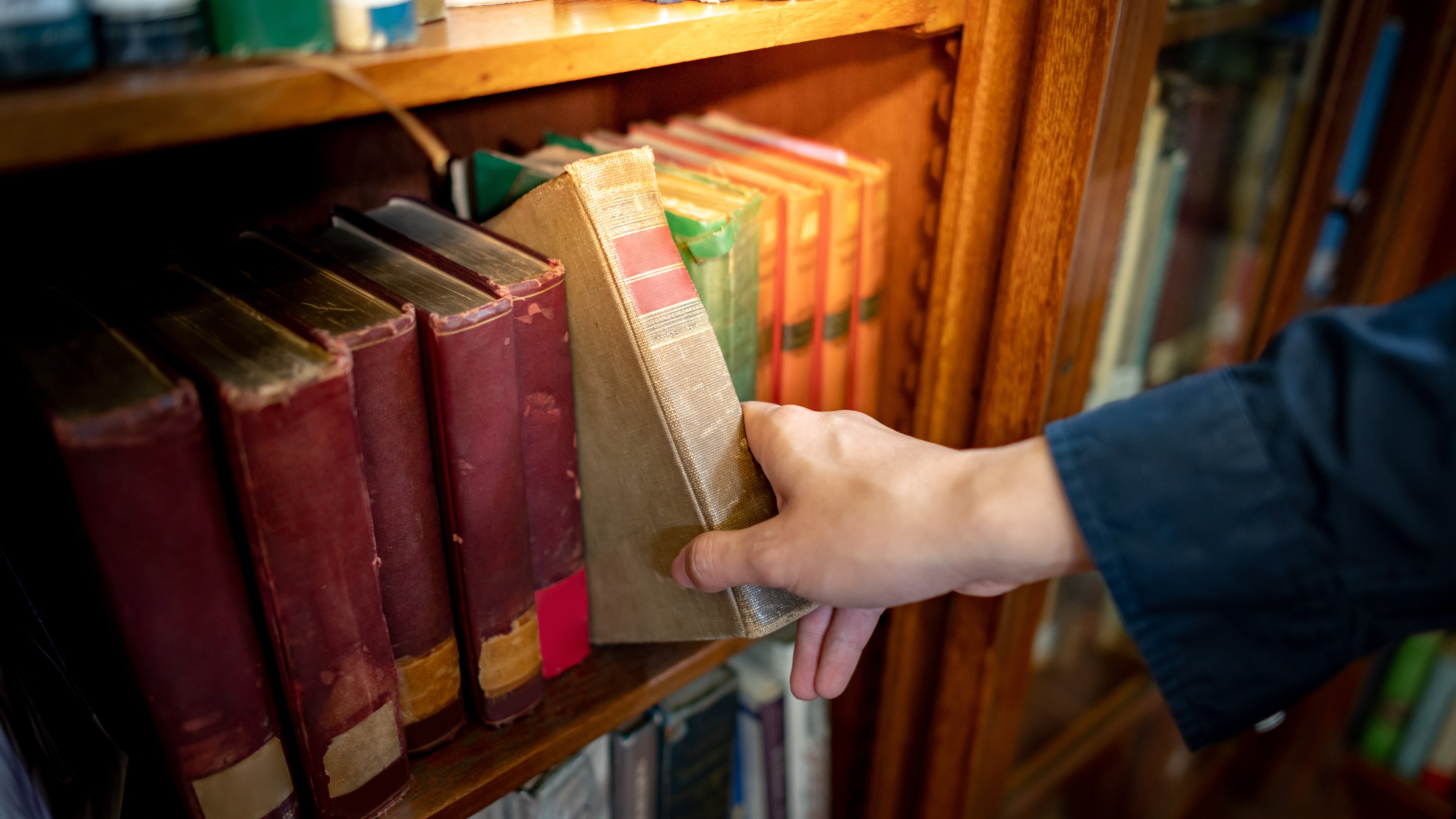 Person reaching for a worn book on a bookshelf