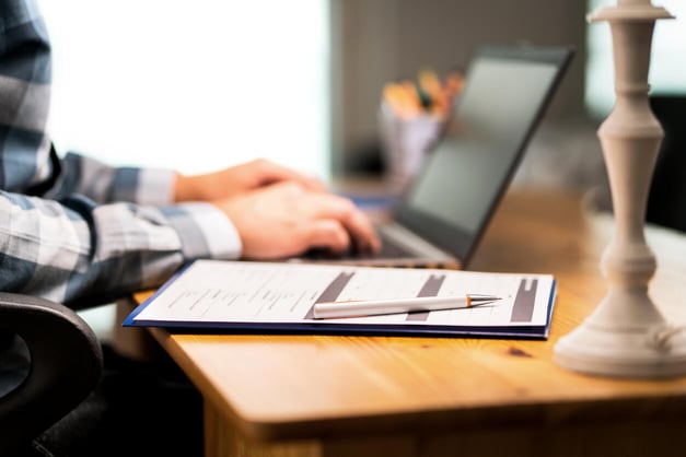 person typing on laptop with a form on the table beside them